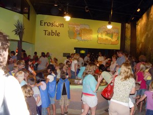 This room, which smells heavily of chlorine, has a big wrap-around table filled with water and sand. Kids can build dams and create rivers and streams, complete with plastic dinosaurs and palm trees. I suppose on a slower day they could watch as the water washed away their dams and moved the dinosaurs and trees around, but it was packed when we went. See that crowd? Bleh.